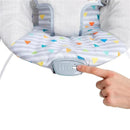 Bright Starts Baby Bouncer with soothing vibrations, featuring a colorful patterned seat and a finger pressing the control button.