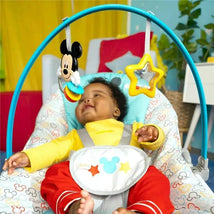 Infant in a Bright Starts Disney Baby Mickey Mouse rocker, smiling at hanging toys featuring Mickey Mouse and a star.