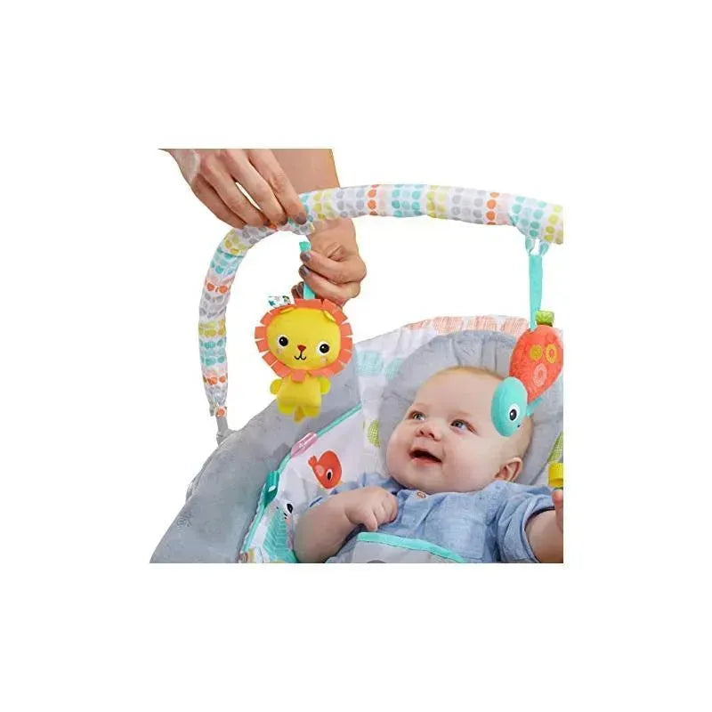 A smiling baby in a cradling bouncer looks up at a colorful lion toy hanging from an arch.