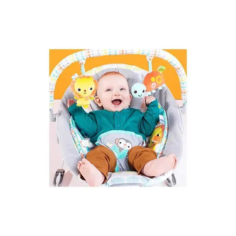 Baby smiling while seated in the Bright Starts Whimsical Wild Cradling Bouncer, holding plush toys of a lion and a colorful fruit.