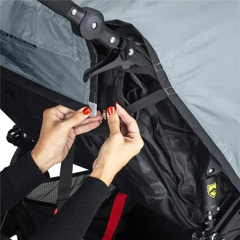 A person with red nails adjusts the weather shield on a Britax Duallie Swivel Wheel Stroller, showcasing its features.