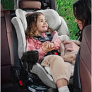 Child in a Romer Veni Convertible Car Seat, Pearl, smiling while holding a stuffed toy, with a caregiver interacting beside her.