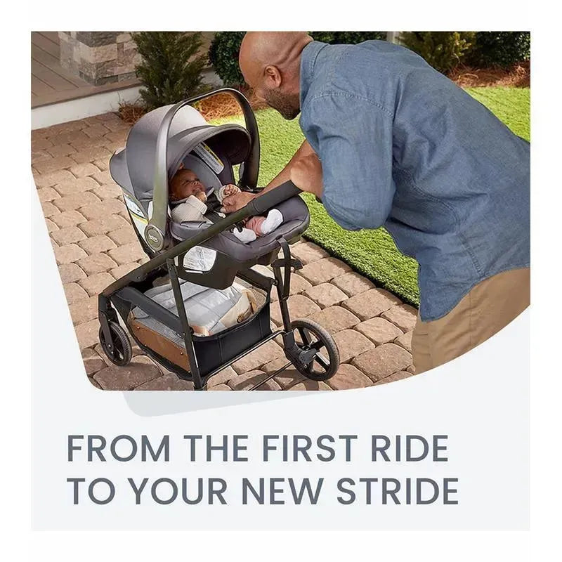 A man interacts joyfully with a baby in the Britax Willow Brook Travel System stroller, set on a stone pathway with grass nearby.