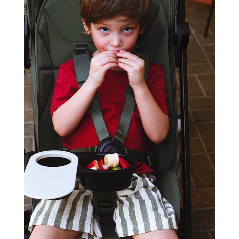 Child sitting in a Bugaboo stroller with a food and drink tray, enjoying snacks including fruit.