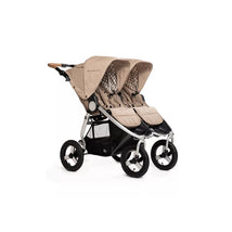 Double stroller in sand color with two canopies, cushioned seats, and a silver frame, designed for infants and toddlers.