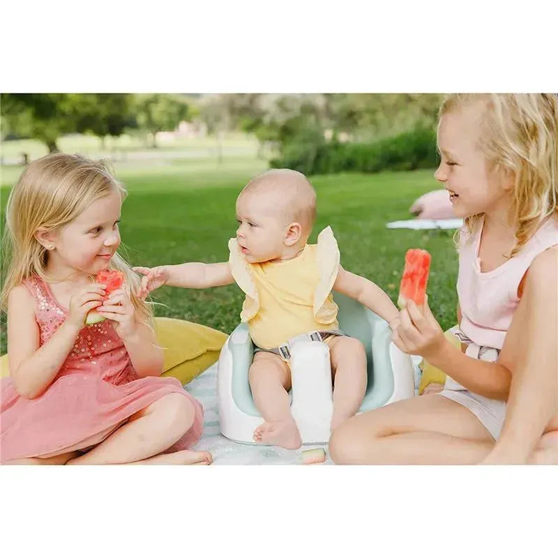 Three children enjoy watermelon slices outdoors; a baby in a taupe Bumbo multi-seat reaches for one slice.