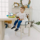 Child seated in a Bumbo taupe adjustable height 3-in-1 multi-seat at a table, playing with a colorful activity toy.