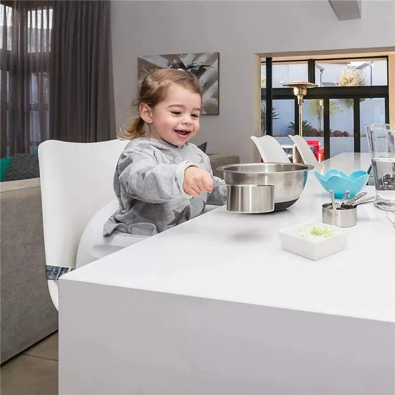 Child happily playing with a metal bowl on a white table, seated in a Bumbo Taupe Adjustable Height 3-in-1 Multi Seat.