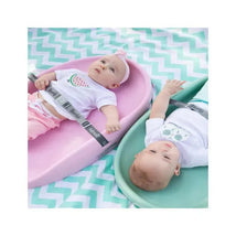 Two babies are reclining on Bumbo changing pads in pink and green, wearing matching shirts with playful designs on a chevron-patterned blanket.