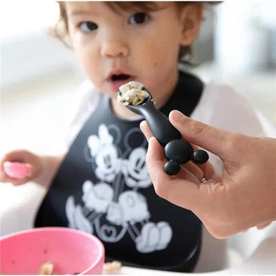 Silicone dipping spoon featuring Mickey Mouse design, held by an adult feeding a toddler in a high chair.