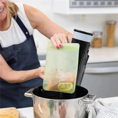 Hands placing a green silicone reusable bag with chicken and lemon slices into a pot, featuring a sous vide precision cooker.