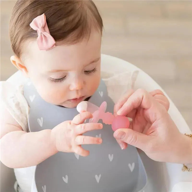 Baby using Bumkins Chewtensils Silicone utensils in pink jelly color, held by an adult hand during mealtime.