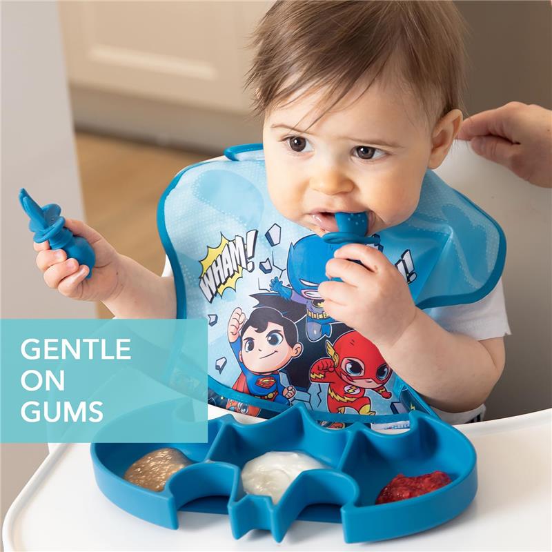 Baby using Bumkins Batman-shaped silicone spoon set, featuring colorful purees in a divided tray and a bib with superhero design.