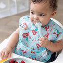 Baby wearing a Disney Ariel bib, holding a light blue spoon, with fruit on a plate nearby.