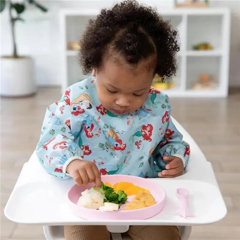 Child in a high chair using a Bumkins Disney silicone plate and spoon set, eating rice, broccoli, and squash.