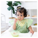 A young child wearing a green Bumkins Disney Tiana-themed ruffle apron bib smiles while eating from a bowl.