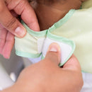 Green Disney Tiana ruffle apron bib being fastened, showing Velcro closure and fabric details.