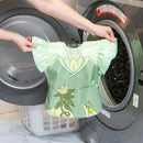 Bumkins Disney Ruffle Apron Bib in green, featuring a Tiana design, being held next to a washing machine.