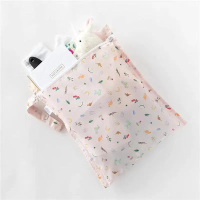 Disney-themed Bumkins waterproof wet bag in soft pink, featuring colorful animal and floral patterns, filled with a notebook and plush toy.