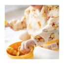 Bumkins Disney Winnie the Pooh sleeved bib on a child, who is playing with a yellow bowl and toys inside.