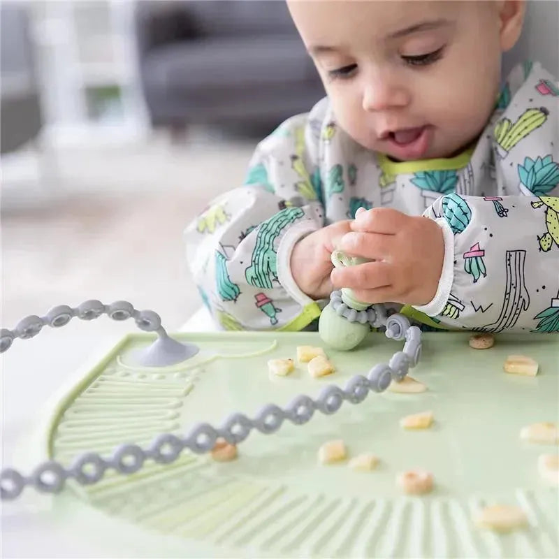Gray silicone accessory tethers on a green mat, with a baby playing and manipulating small items.