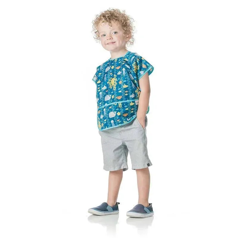 Bumkins Junior Bib in a colorful ocean theme, worn by a smiling child with curly hair, paired with light shorts.