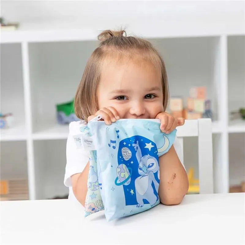 A young child smiles while holding a Bumkins large snack bag featuring a Stitch design with space and musical themes.