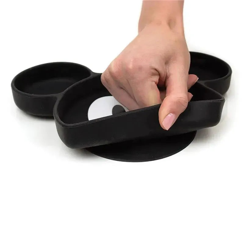 Black silicone grip dish in the shape of Mickey Mouse, featuring separate sections for food. Hand is grasping the dish.