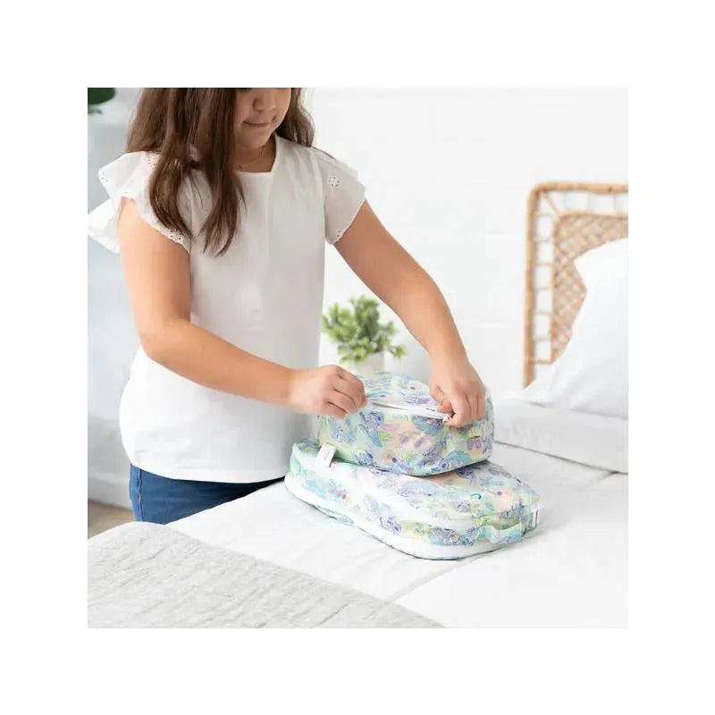 Girl organizing two Bumkins packing cubes with a colorful Aloha design on a bed.