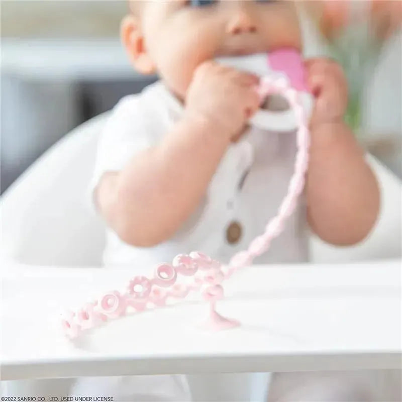 Pink silicone accessory tethers designed for infants, with a baby gripping a connector while sitting at a table.