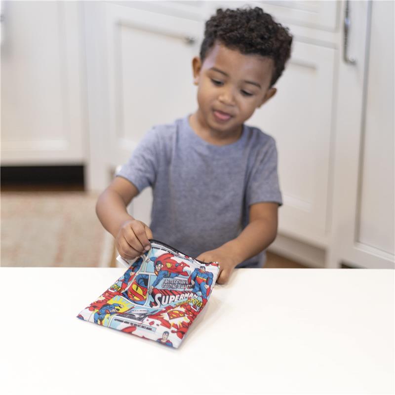 A child is using a Bumkins DC Comics Superman reusable sandwich bag, featuring vibrant superhero graphics.