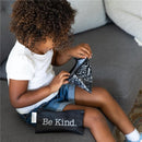 Child exploring a Bumkins reusable snack bag, featuring a black design with positive words, while sitting on a couch.