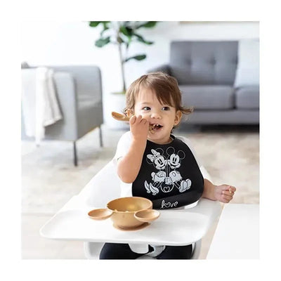 Silicone bib featuring Mickey and Minnie Mouse designs, worn by a young child eating from a golden bowl.