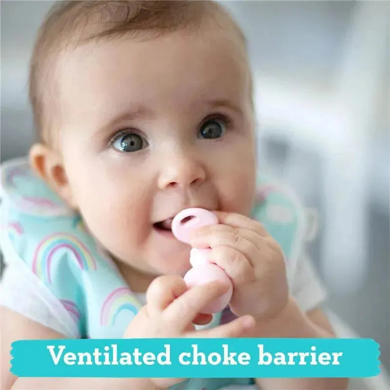 Baby holding a pink silicone utensil with a ventilated choke barrier, wearing a colorful bib and smiling.