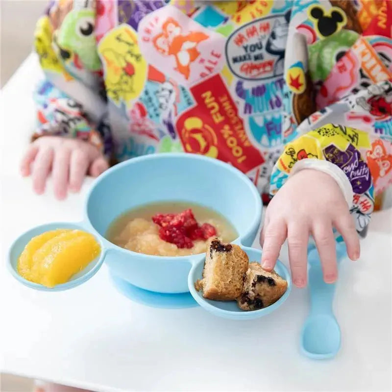 Silicone feeding set in light blue featuring a bowl with applesauce, raspberries, and side compartments with fruit and cake.