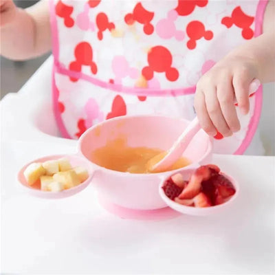 Silicone feeding set featuring a light pink bowl with suction, accompanied by fruit compartments and a matching spoon.