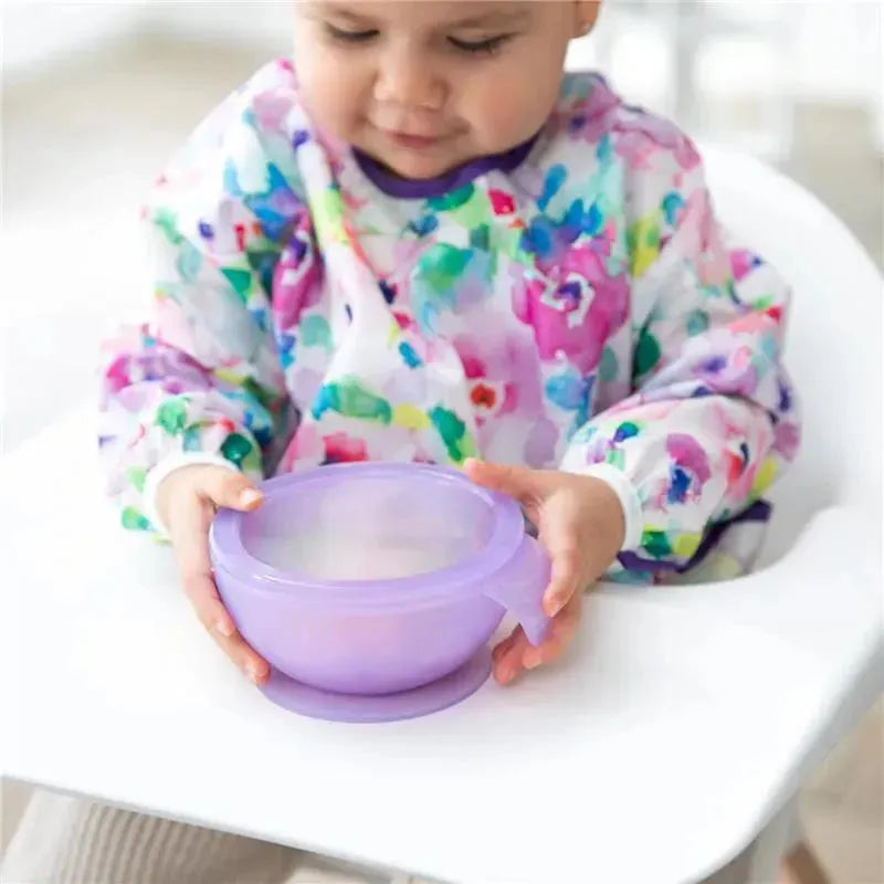 Toddler wearing a colorful bib holds a purple silicone feeding bowl with suction, designed for mess-free meals.