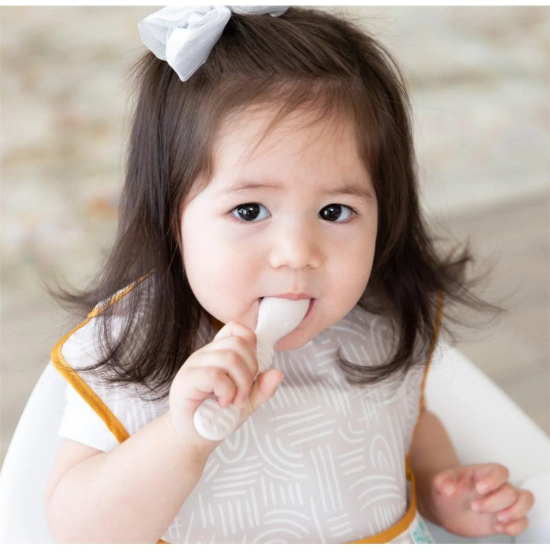 Bumkins Silicone First Feeding Set in sand color, featuring a toddler holding a spoon, wearing a bib.