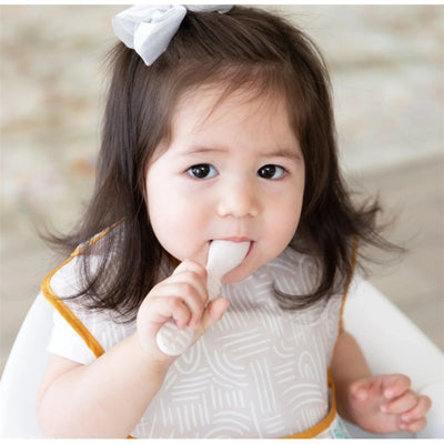 Bumkins Silicone First Feeding Set in sand color, featuring a toddler holding a spoon, wearing a bib.