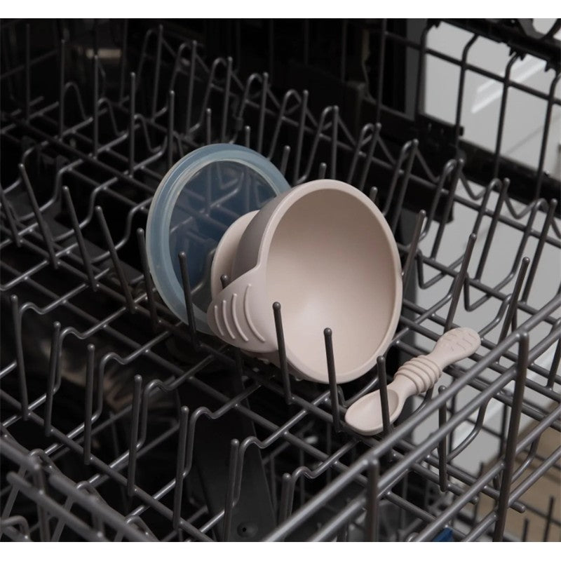 Bumkins Silicone First Feeding Set in sand color, featuring a bowl with lid and spoon, positioned in a dishwasher.