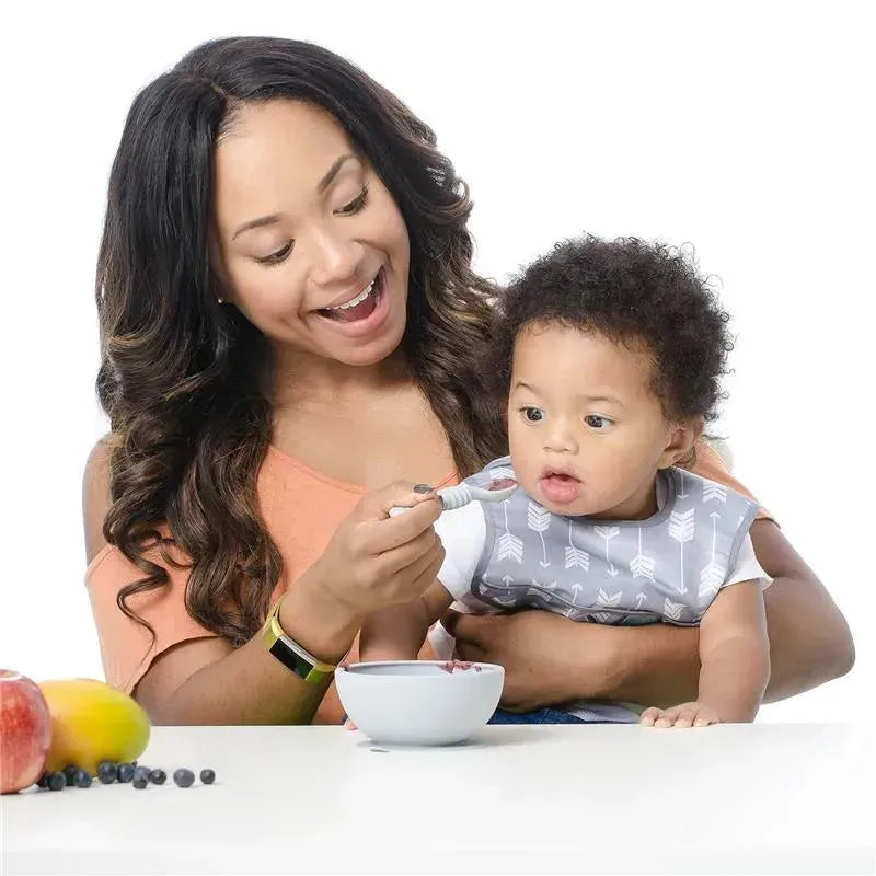 Woman feeding a baby with a spoon from a bowl, showcasing the Bumkins Silicone First Feeding Set in gray.
