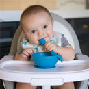Gray silicone feeding set with lid and spoon, featuring a baby happily holding the spoon and bowl.