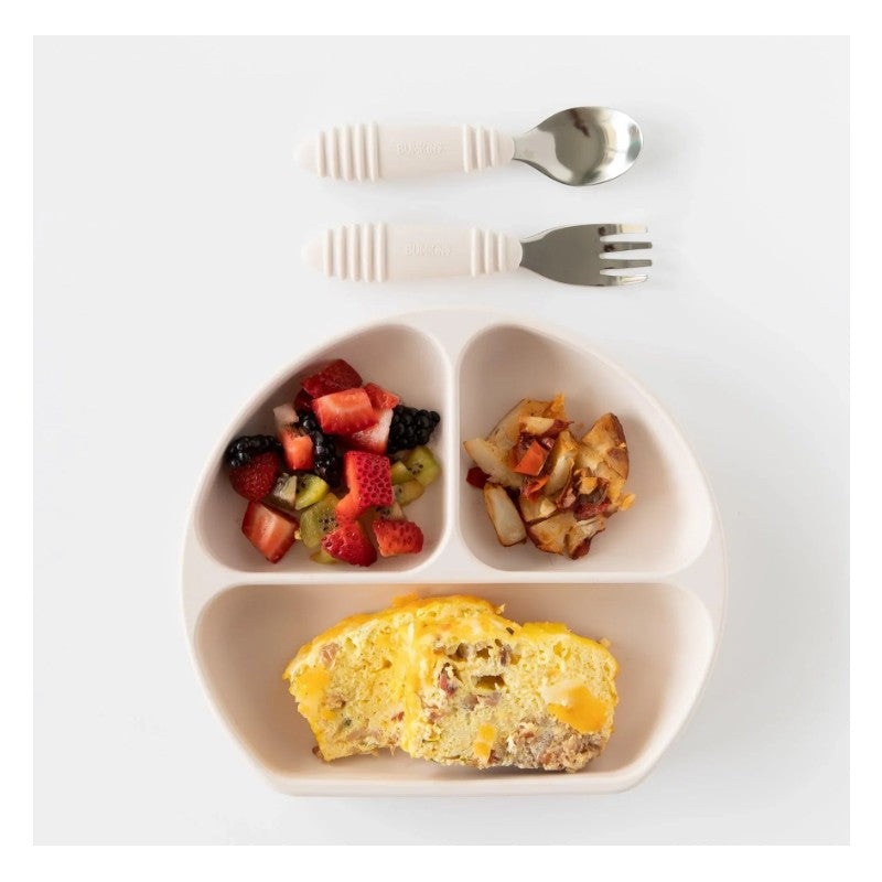 Bumkins Silicone Grip Dish in sand color with three food sections holding fruit, omelet, and potatoes, accompanied by child-friendly utensils.