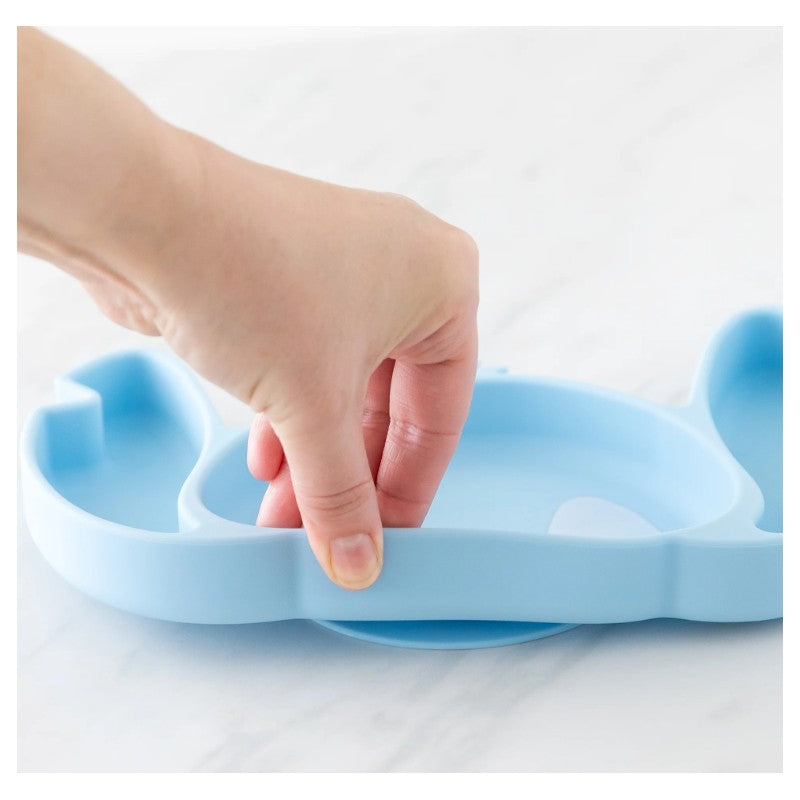 Hand holding a light blue Bumkins silicone grip dish shaped like Stitch, positioned on a white surface.