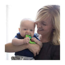 Baby happily chewing on a green dinosaur-shaped silicone teether while being held by a smiling woman.