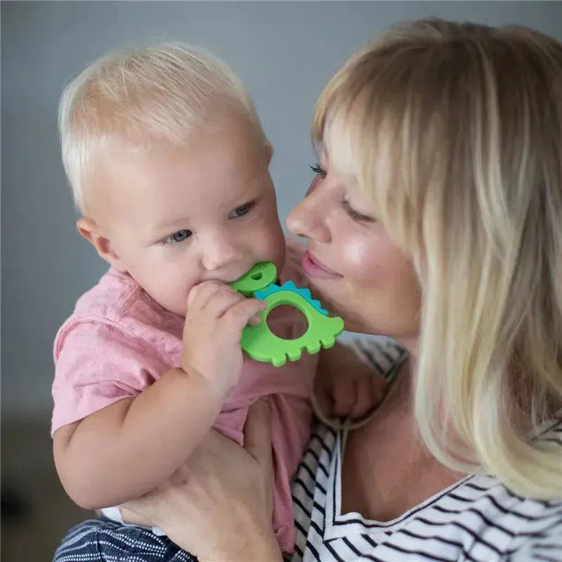 A child holding a green dinosaur-shaped silicone teether, being comforted by a smiling adult.