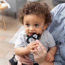 Silicone teether shaped like Mickey Mouse, being held by a child who is smiling while chewing on it.