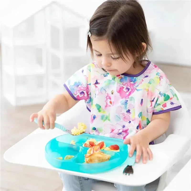 A young child with a colorful floral shirt uses a silicone blue dish to eat scrambled eggs and cherry tomatoes.