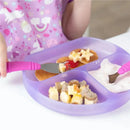 Purple silicone dish with three sections filled with pancakes, fruit, and yogurt, being eaten by a child using pink utensils.