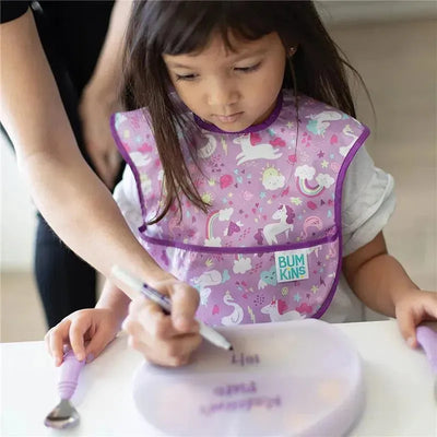 Toddler wearing a lavender Bumkins bib with unicorns, drawing with a marker on a clear suction plate.